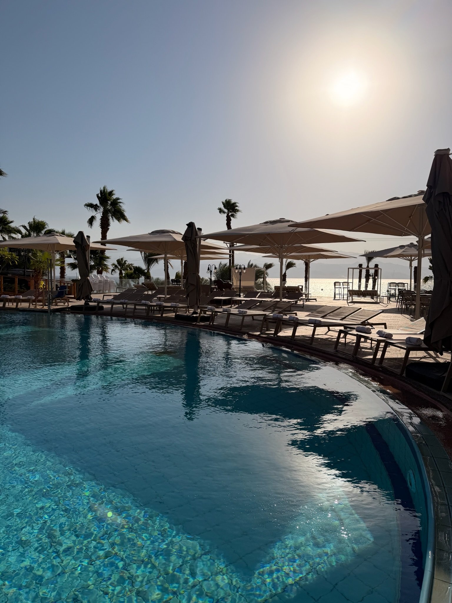 The pool at midday, the sun above the parasols